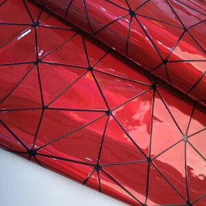 May include: Close-up of a glossy, red material with a geometric design. Black lines form a triangular pattern across the surface. The material reflects light, creating highlights. The overall effect is a shiny, textured surface.