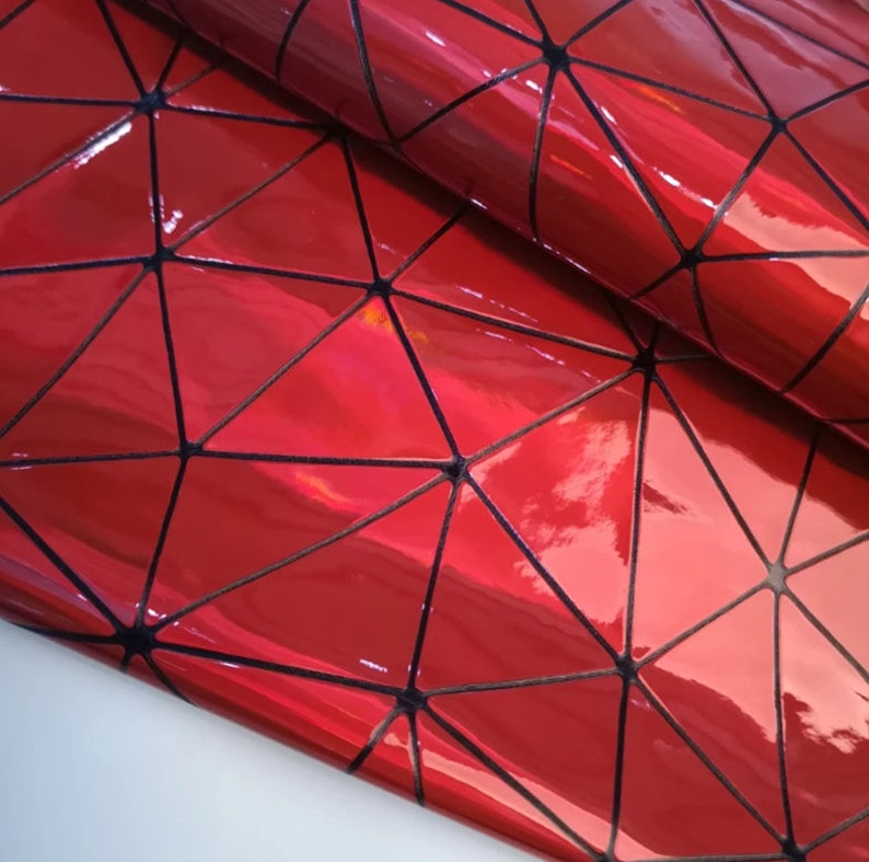 May include: Close-up of a glossy, red material with a geometric design. Black lines form a triangular pattern across the surface. The material reflects light, creating highlights. The overall effect is a shiny, textured surface.
