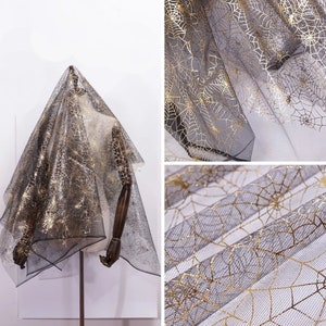 May include: Black and gold spiderweb fabric draped over a mannequin. The sheer material features a delicate gold spiderweb pattern against a black background. The fabric is displayed in multiple views, showcasing its texture and design.