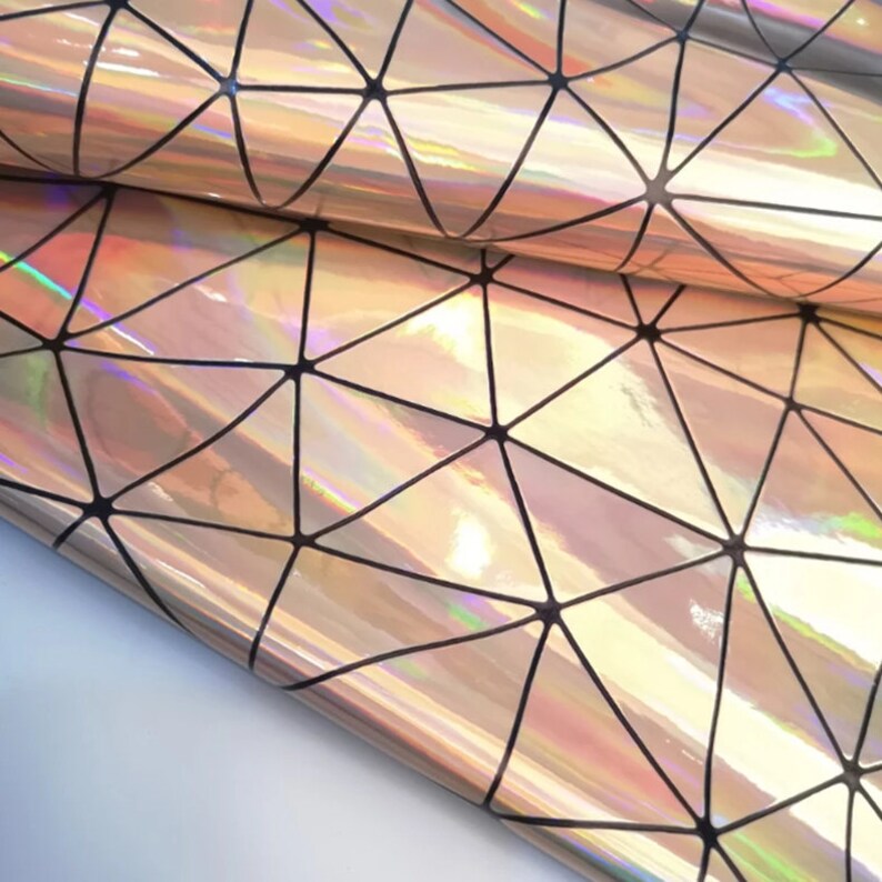May include: Holographic material with a geometric triangular pattern. The material reflects pink, gold, and green. Black lines form a network of triangles across the surface. The material appears to be folded.
