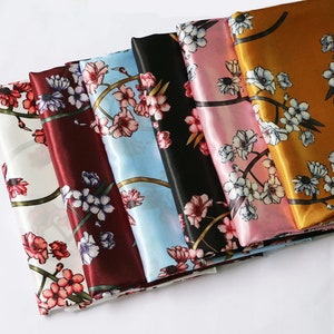 K&ouml;nnte beinhalten: Eine Sammlung von Seidenschals in verschiedenen Farben, jeweils mit einem floralen Muster verziert. Die Schals zeigen eine Reihe von Farbt&ouml;nen, darunter Wei&szlig;, Burgunderrot, Schwarz, Hellblau, Rosa und Gold. Das florale Design zeigt rosa und wei&szlig;e Bl&uuml;ten.