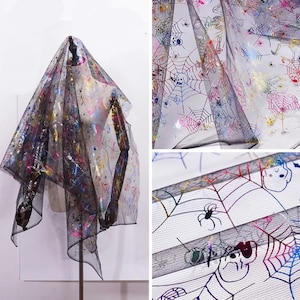 May include: Black sheer fabric with a Halloween design. The fabric is decorated with colourful spiderwebs, spiders, and skeleton graphics. The fabric is draped over a mannequin, showing its texture and pattern.