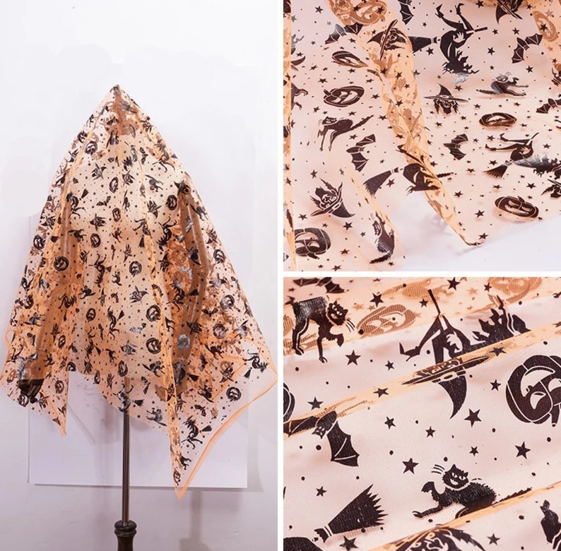 May include: Peach-coloured, sheer Halloween fabric featuring black silhouettes of bats, cats, witches, pumpkins, and stars. The fabric is draped over a stand, highlighting its design and texture. The edges are finished with a peach border.