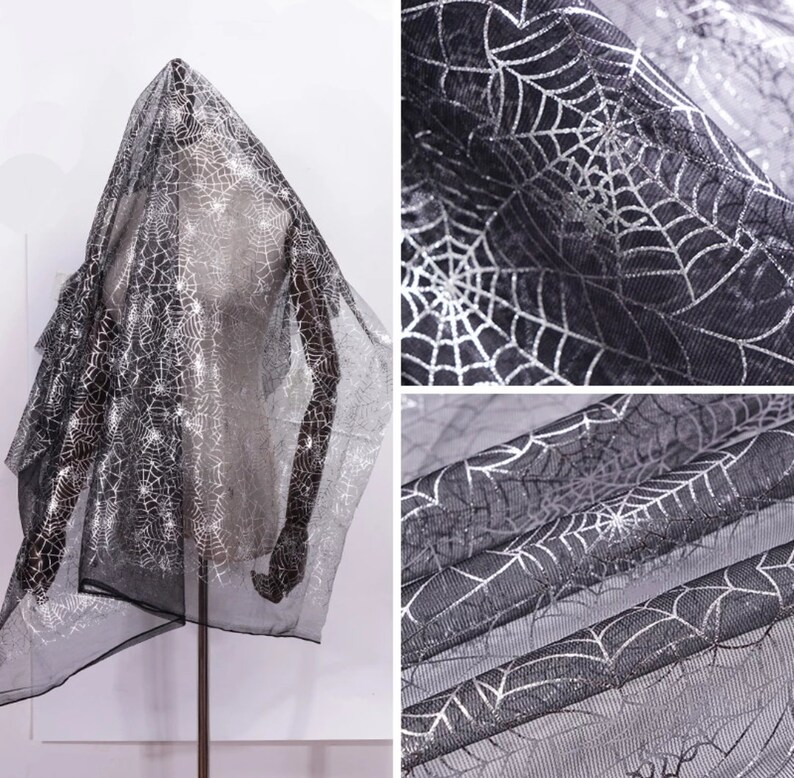 May include: Black, sheer fabric featuring a silver spiderweb design. The material is draped over a mannequin, highlighting the intricate pattern. Suitable for Halloween or themed occasions.