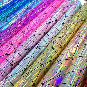 May include: A selection of holographic paper rolls in various colours. The rolls feature a geometric pattern of black lines over a rainbow of colours, including pink, blue, and gold. The paper has a shiny, reflective surface.