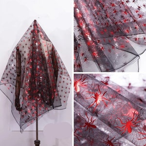 May include: Black sheer fabric decorated with red and silver spider motifs. The material is displayed over a mannequin, highlighting its texture and design. Suitable for Halloween decorations or themed crafts.