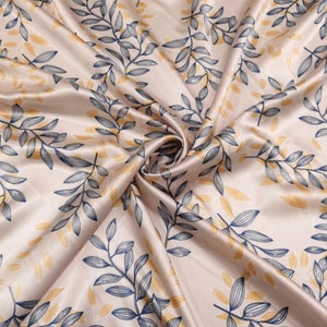 May include: Satin fabric with a repeating pattern of stylized leaves. The leaves are in shades of navy blue and gold against a pale beige background. The fabric is draped, showing folds and texture.