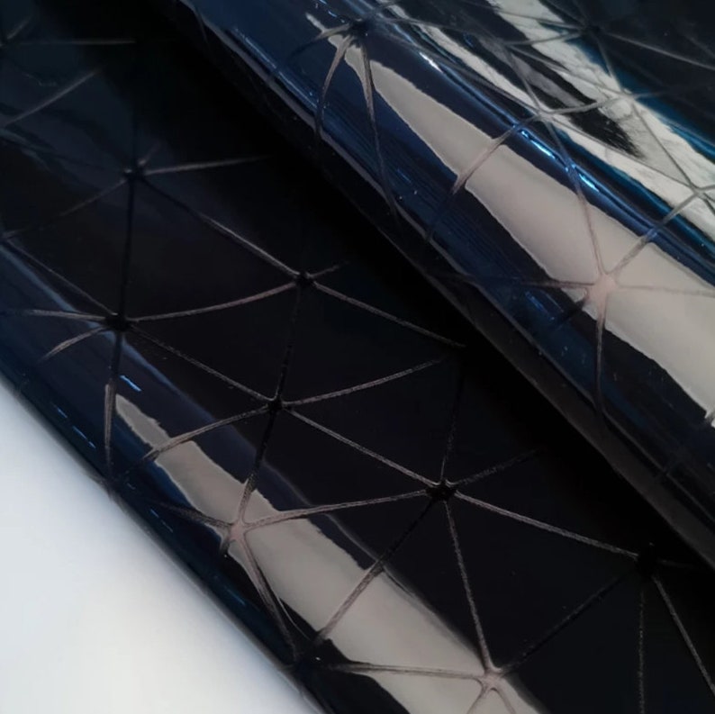 May include: Close-up of a glossy, black material with a geometric pattern of interconnected triangles. The surface reflects light, creating highlights and shadows. The material appears to be folded or draped.