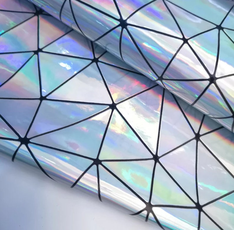 May include: Iridescent geometric patterned fabric. The material has a shiny, reflective surface with a repeating pattern of triangles outlined in black. The fabric reflects a rainbow of colours, creating a holographic effect.