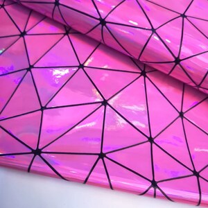 May include: Close-up of a sheet of pink, iridescent material with a geometric pattern. Black lines form triangles and other shapes. The material has a shiny, reflective surface, with a slight sheen.