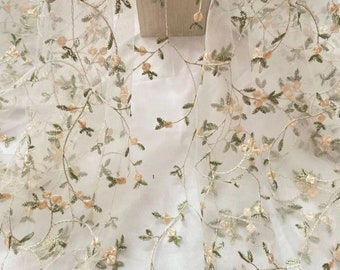May include: Delicate ivory fabric with embroidered floral vines. The design features small peach-colored rosebuds and green leaves, creating a soft, romantic pattern. The sheer material is ideal for bridal or decorative projects.
