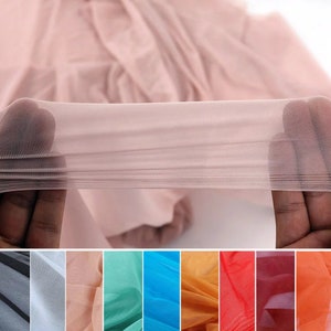 May include: A close-up of sheer, light pink fabric stretched between two hands. The fabric is semi-transparent, revealing a glimpse of the background. Below, a color palette of various sheer fabrics in shades of gray, pink, teal, blue, orange, and red.