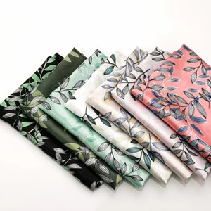 May include: A collection of folded fabric squares in various colors, each adorned with a delicate leaf pattern. The color palette includes black, dark green, mint green, white, and pink. The leaves are depicted with fine lines, creating a detailed and elegant design.