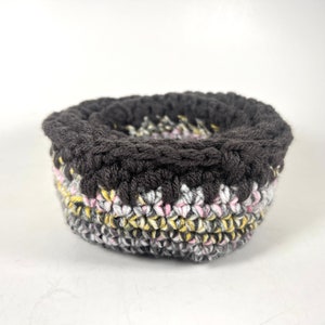 May include: A crocheted bowl with a black top and a multi-colored bottom with pink, yellow, and gray yarn.