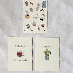 Könnte beinhalten: Drei illustrierte Karten mit Kaffeemotiven. Eine Karte zeigt verschiedene Kaffeebilder und den Text "COFFEE DATE?". Eine andere Karte hat eine Kaffeetassenillustration und deutschen Text. Die dritte Karte zeigt eine Kaffeemaschinenillustration und deutschen Text.