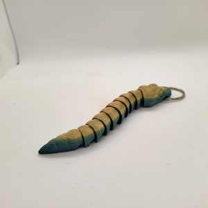 以下が含まれることがあります： ミミズまたはイモムシの形をした、セグメント化された青と黄色の木製キーホルダー