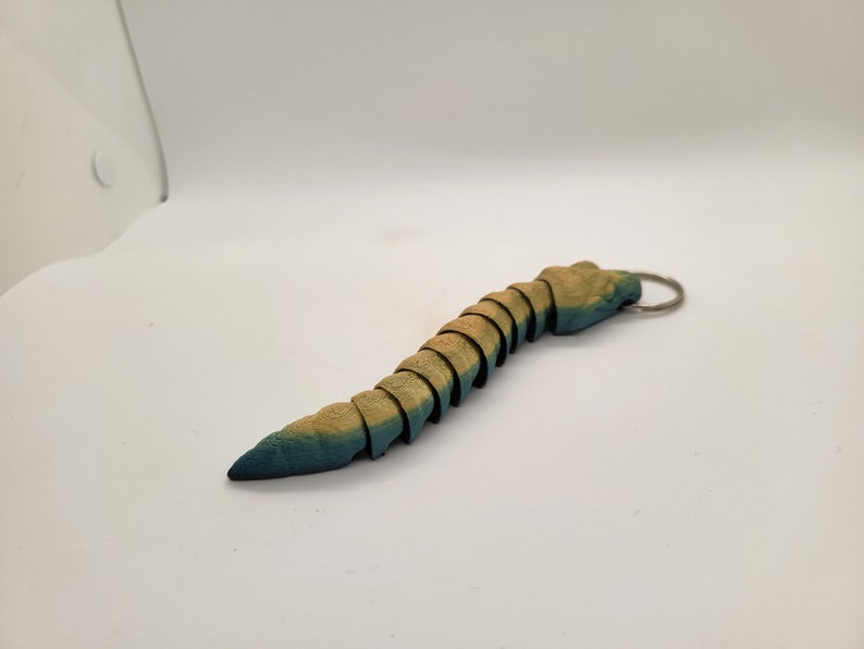 以下が含まれることがあります： ミミズまたはイモムシの形をした、セグメント化された青と黄色の木製キーホルダー