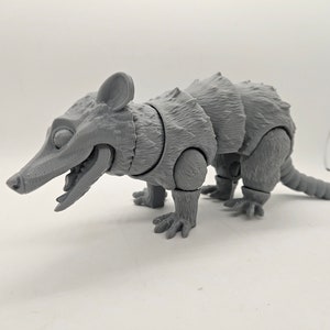 May include: A gray 3D printed model of an armadillo with articulated limbs. The model is posed in a walking position with its mouth open.