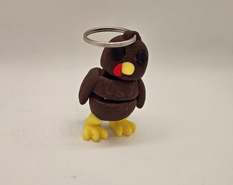 May include: A brown and yellow 3D printed turkey keyring with a silver ring. The turkey has black eyes and a red beak.