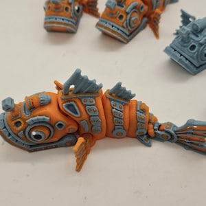 Op de afbeelding: Een gedetailleerd, oranje en blauw, 3D-geprint visfiguurtje met ingewikkelde ontwerpen en een gesegmenteerd lichaam.