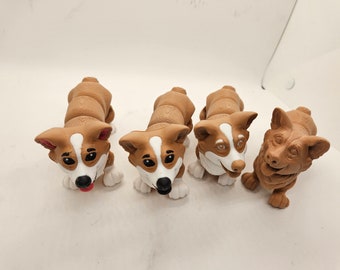 May include: Four brown and white corgi dog figurines. The figurines are made of a smooth, brown material and have white markings on their faces. They are all looking at the camera.