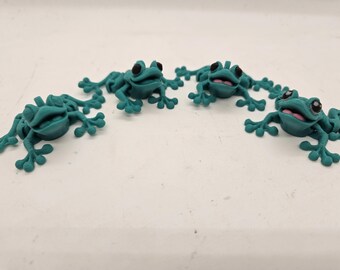 Peut inclure: Quatre figurines de grenouilles vert turquoise avec des yeux noirs et des sourires blancs. Les grenouilles sont disposées en demi-cercle.