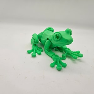May include: A green 3D printed frog figurine with articulated limbs. The frog has large eyes and a detailed textured surface.