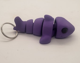 Könnte beinhalten: Ein lilafarbener 3D-gedruckter Hai-Schlüsselanhänger mit einem silbernen Ring. Der Hai ist segmentiert und hat ein schwarzes Auge.