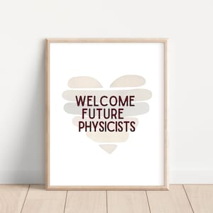 May include: A framed print with a white background and a heart shape made of beige and gray watercolor. The text "WELCOME FUTURE PHYSICISTS" is written in maroon inside the heart.