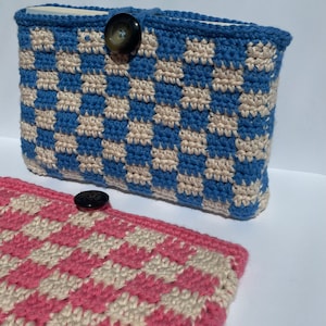 Op de afbeelding: Twee gehaakte ritszakjes met geruite patronen. Eén zakje is blauw en wit, de andere is roze en wit. Beide zakjes hebben een knoopsluiting.