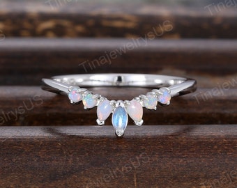 May include: A delicate silver ring with a curved row of oval-shaped opal gemstones. The ring is set on a wooden surface.