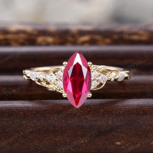 Peut inclure: Une bague en or ornée d'un grand rubis de forme marquise, d'un rouge vif. L'anneau est orné de petits diamants transparents et de motifs délicats en forme de feuilles, pour un bijou raffiné.