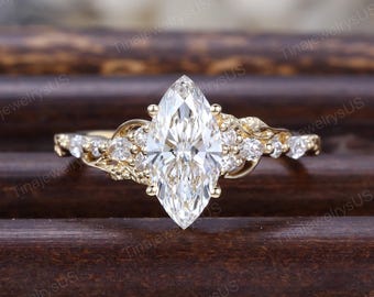 May include: A yellow gold ring featuring a large marquise-cut centre stone flanked by smaller round-cut stones on each side. The band has a textured, organic design that branches out from the centre setting, holding the stones in place.