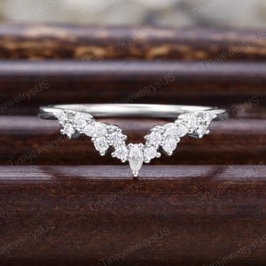 Puede incluir: Un anillo plateado con un dise&ntilde;o curvo, adornado con m&uacute;ltiples piedras preciosas claras y brillantes. El anillo presenta una piedra central con corte marquesa, rodeada de piedras m&aacute;s peque&ntilde;as, de corte redondo, creando una apariencia delicada y elegante.