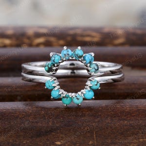 May include: A silver ring set with a halo of turquoise stones. The ring features a double band design, with the turquoise stones arranged in a circular pattern. The stones are a vibrant blue-green color.