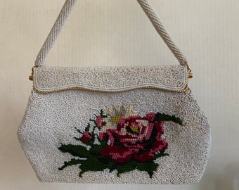 Könnte beinhalten: Eine weiße Perlenhandtasche mit einem goldenen Verschluss und einem Blumendesign mit einer rosa Rose.