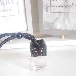 May include: A black car air freshener with a decorative metal cage and a clear glass bottle. The air freshener is hanging from a black string.