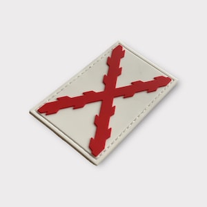 Puede incluir: Parche blanco con una cruz roja con un diseño de borde dentado. El parche tiene un borde blanco con un borde cosido.