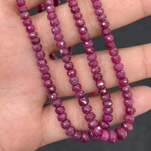 May include: Strands of faceted, deep red ruby beads. The beads are strung together, creating a necklace or bracelet. The gemstones have a polished, reflective surface, and are displayed against a neutral background.