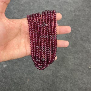 May include: A strand of deep red gemstone beads. The beads are round and smooth, and they are strung on a clear thread. The beads are approximately 4mm in diameter.