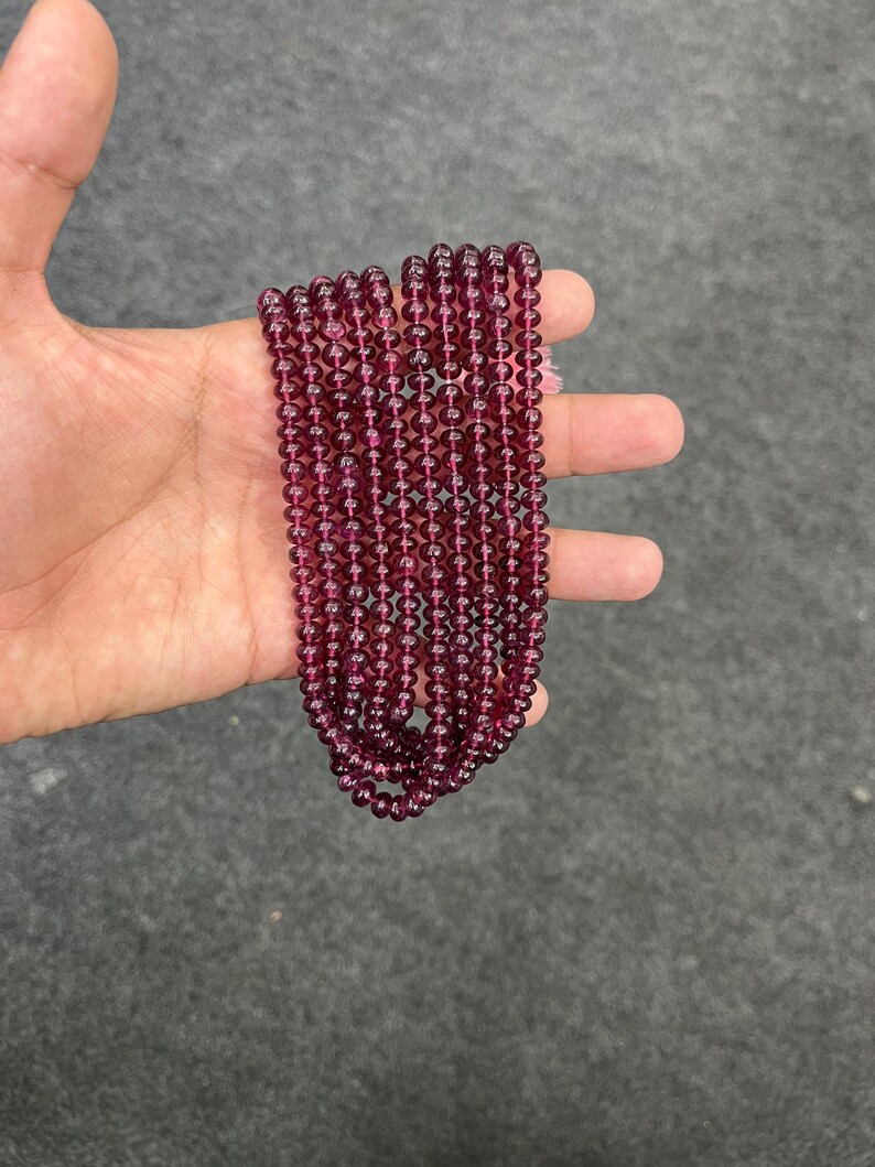May include: A strand of deep red gemstone beads. The beads are round and smooth, and they are strung on a clear thread. The beads are approximately 4mm in diameter.