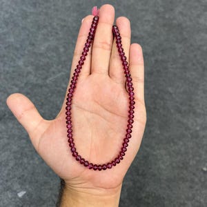 May include: A strand of deep red gemstone beads, strung on a thin cord. The beads are round and smooth, and the strand is approximately 18 inches long.