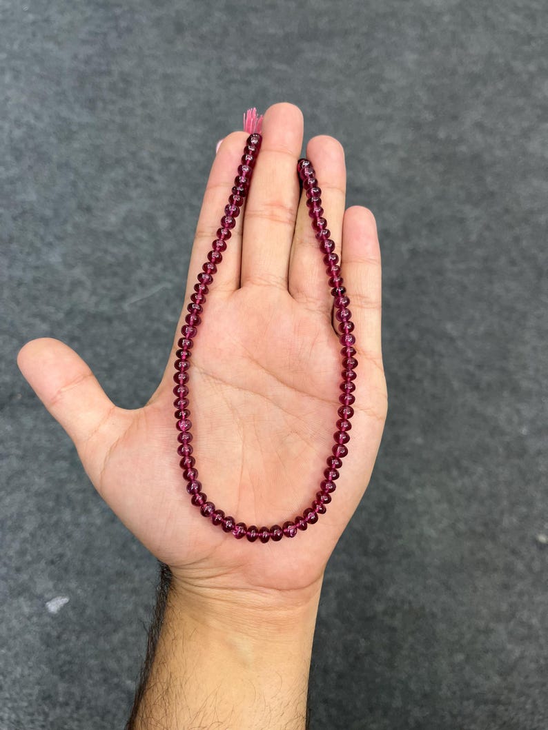 May include: A strand of deep red gemstone beads, strung on a thin cord. The beads are round and smooth, and the strand is approximately 18 inches long.