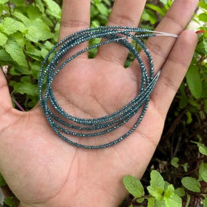 K&ouml;nnte beinhalten: Eine Str&auml;hne blauer Diamantperlen, die auf einem Silberdraht aufgef&auml;delt sind. Die Perlen sind klein und rund und haben eine funkelnde, facettierte Oberfl&auml;che.