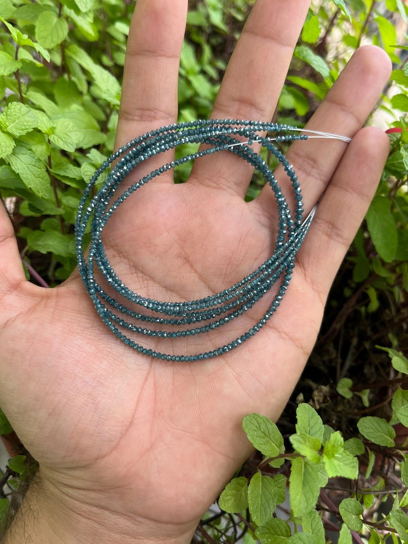 K&ouml;nnte beinhalten: Eine Str&auml;hne blauer Diamantperlen, die auf einem Silberdraht aufgef&auml;delt sind. Die Perlen sind klein und rund und haben eine funkelnde, facettierte Oberfl&auml;che.