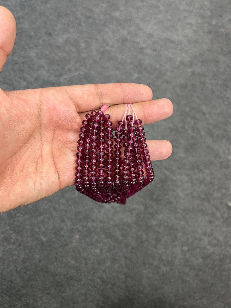 May include: A strand of deep red gemstone beads, likely garnet, strung on a thin pink thread. The beads are round and uniform in size, creating a smooth and elegant look.