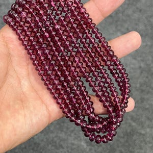 May include: A strand of deep red gemstone beads. The beads are round and smooth, and they are strung on a clear thread. The beads are approximately 4mm in diameter.