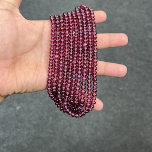 May include: A strand of deep red gemstone beads. The beads are round and smooth, and they are strung on a clear thread. The beads are approximately 4mm in diameter.