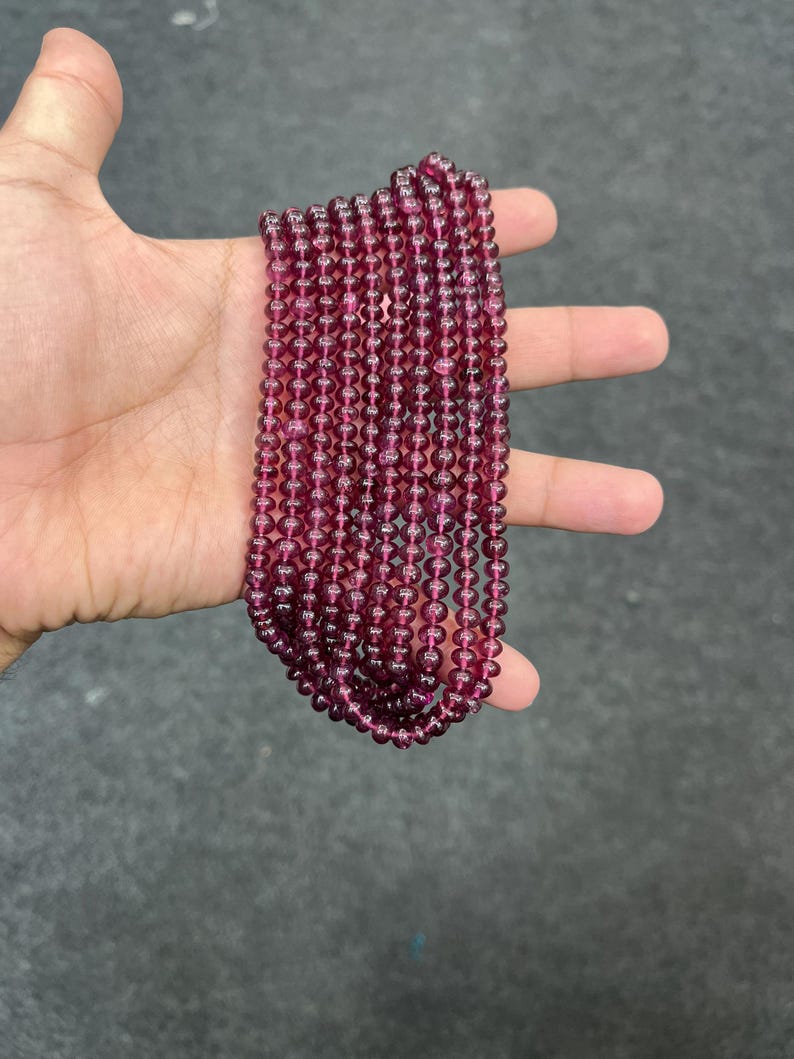 May include: A strand of deep red gemstone beads. The beads are round and smooth, and they are strung on a clear thread. The beads are approximately 4mm in diameter.