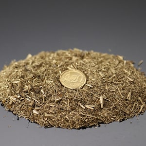 May include: A mound of small, gold-coloured metal shavings with a gold-coloured coin on top. The coin has the number "20" on it. The shavings are scattered on a dark, reflective surface.